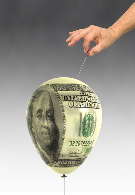 Orchestrated balloon printed with a dollar bills about to be popped.